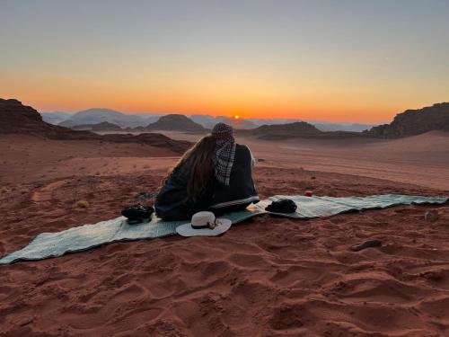 a person sitting in the desert watching the sunset at desert colored camp in Wadi Rum