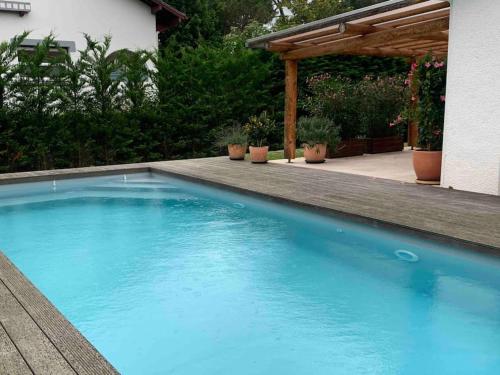 een blauw zwembad in een achtertuin met een pergola bij Villa proche océan et golf in Anglet
