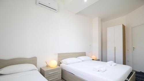 two beds in a bedroom with white walls and two lamps at Appartamento il Maestrale Casa Vacanza in Càbras