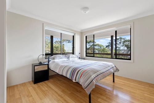 a white bedroom with a bed and two windows at Sapphire Views - Narrawallee Beach in Narrawallee