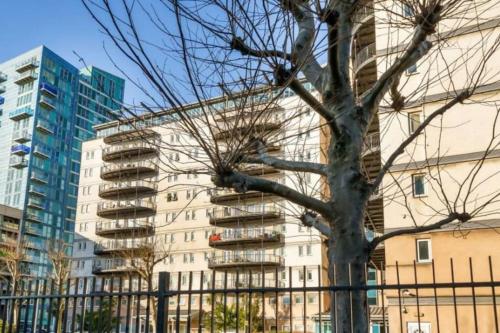 a building with a tree in front of a fence at Stratford Apartment - walk to ABBA Voyage in London
