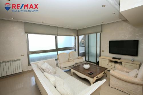 uma sala de estar com mobiliário branco e uma televisão de ecrã plano em פנינה על הים em Netanya