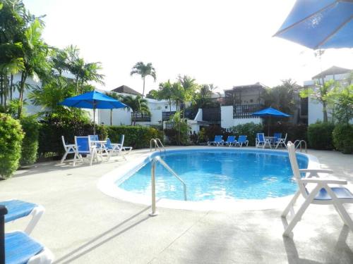 a large swimming pool with chairs and umbrellas at Studio apartment in heart of south coast Barbados in Bridgetown