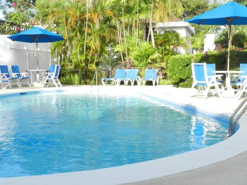 una piscina con sillas y sombrillas azules en Studio apartment in heart of south coast Barbados en Bridgetown
