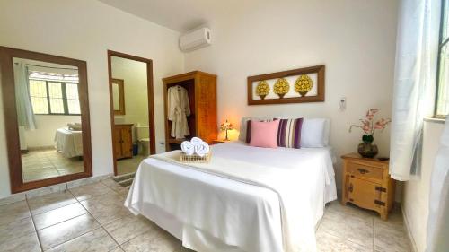 a bedroom with a white bed and a mirror at Pouso das Flores -350m Maria Fumaça in Tiradentes