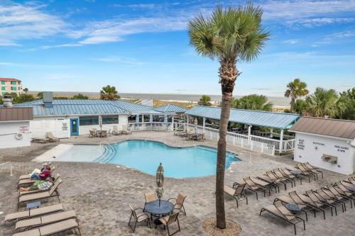 a resort with a pool and chairs and a palm tree at Beach Front Condo w/Pool, Restaurant, and Bar in Tybee Island