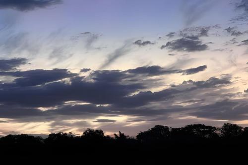 a cloudy sky at sunset with trees in the foreground at Pousada Recanto Janbor in Olímpia