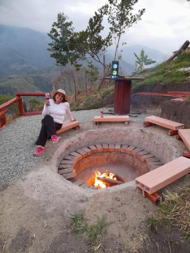 a woman sitting on a bench next to a fire pit at Cabin in the Mountains - Chalet in Ibagué