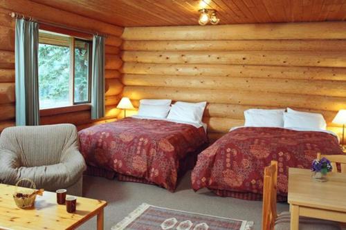 Dormitorio en cabaña de madera con 2 camas y una silla en Terracana Ranch Resort, en Tete Jaune Cache