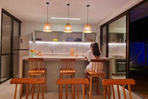 eine Frau, die an einer Theke in einer Küche sitzt in der Unterkunft Kanui VK 102 Milagres - Duplex Perto da Capela e Raizeiros in São Miguel dos Milagres