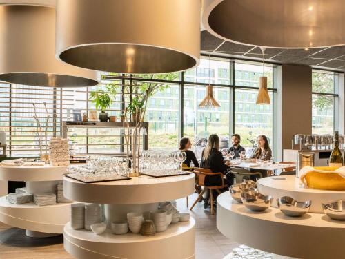 a restaurant with people sitting at tables in a room with large windows at Novotel Paris Coeur d'Orly Airport in Orly