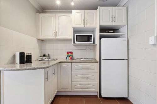 a kitchen with white cabinets and a white refrigerator at Comfy Studio near Gabba with Secure Parking in Brisbane