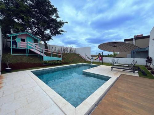 a swimming pool with a table and an umbrella at CASA LIMA, nossa casa na represa in Itaí