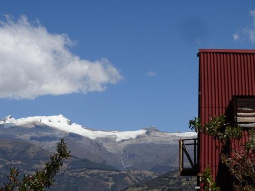 a red building with snow covered mountains in the background at La Teja Experience in Güicán
