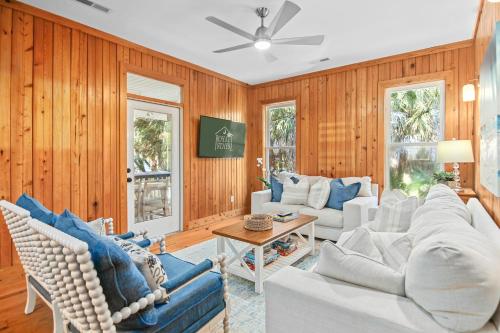 een woonkamer met houten wanden en een bank en stoelen bij Chasing Waves Luxury Edisto Home 3 mins to Beach in Edisto Island