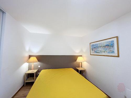 une petite chambre avec un lit jaune et deux lampes dans l'établissement Charmant F2 avec Terrasse, Proche Thermes et Centre-Ville - Animaux Bienvenus, Wifi Inclus - FR-1-451-205, à Lamalou-les-Bains