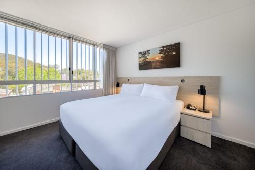 a large white bed in a room with a large window at Oaks Nelson Bay Lure Suites in Nelson Bay