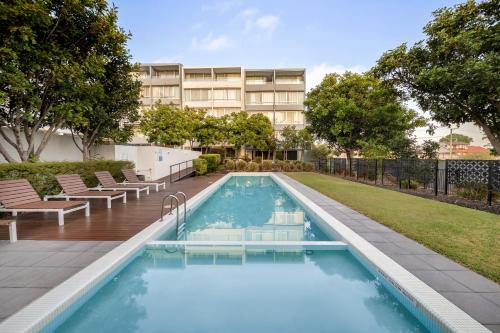 a swimming pool with chairs and a building in the background at Oaks Nelson Bay Lure Suites in Nelson Bay