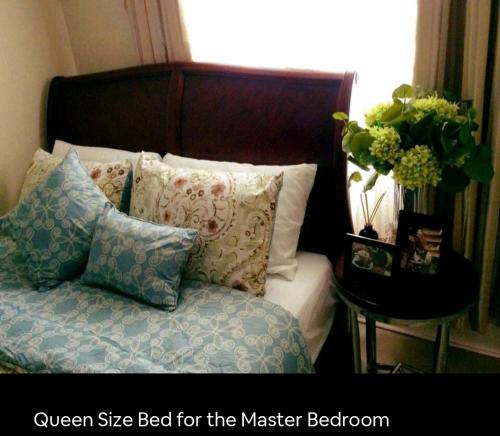 een bed met kussens en een vaas met bloemen op een tafel bij Elegant 2BR Hampton Suites with Pool & WIFI in Anabu Primero