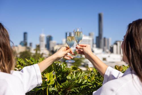 dos mujeres sosteniendo copas de vino frente a una ciudad en Sage Hotel James Street en Brisbane