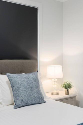 a white bed with a blue pillow and a lamp at South Beach Escape - Sensational Shell Cove Living in Shellharbour