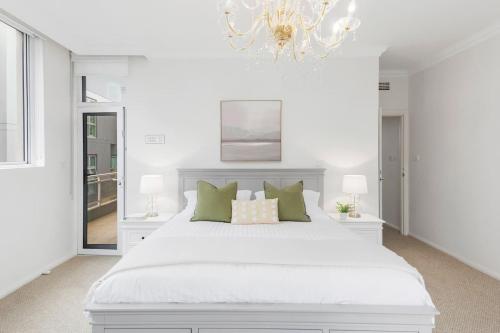 a white bedroom with a white bed and a chandelier at Ocean Vista Escape - A Lofty Beachfront Penthouse in Wollongong
