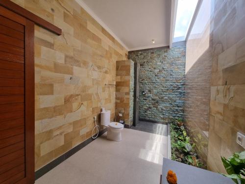 a bathroom with a toilet and a stone wall at Pondok Gadri Villa Ubud in Ubud