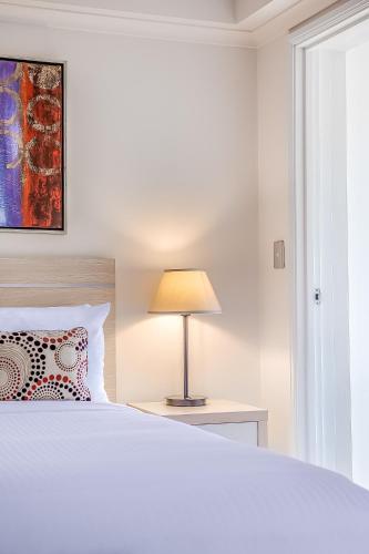 a white bedroom with a bed and a lamp at Oaks Sydney Castlereagh Suites in Sydney