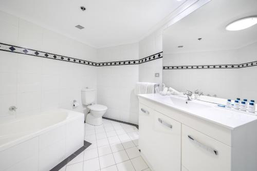 a white bathroom with a tub and a sink and a toilet at Oaks Sydney Castlereagh Suites in Sydney