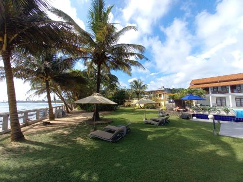 a lawn with chairs and umbrellas next to the ocean at IMAGINE Villa Hotel in Mirissa