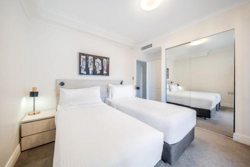 a white bedroom with two beds and a mirror at Oaks Sydney Castlereagh Suites in Sydney