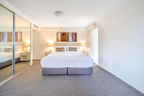 a bedroom with a large white bed and mirrors at Oaks Sydney Castlereagh Suites in Sydney
