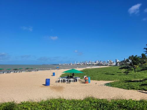 - une plage de sable avec un parasol vert et des chaises dans l'établissement Lindo flat a 50m da praia do Bessa, à João Pessoa