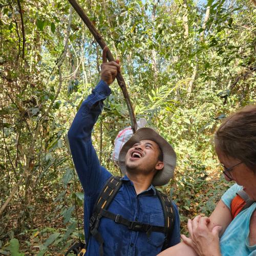 a man in a hat holding a stick in the jungle at Banlung Mountain View Treks & Tours in Banlung