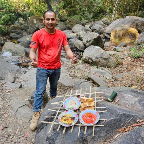 a man standing next to a grill with plates of food at Banlung Mountain View Treks & Tours in Banlung