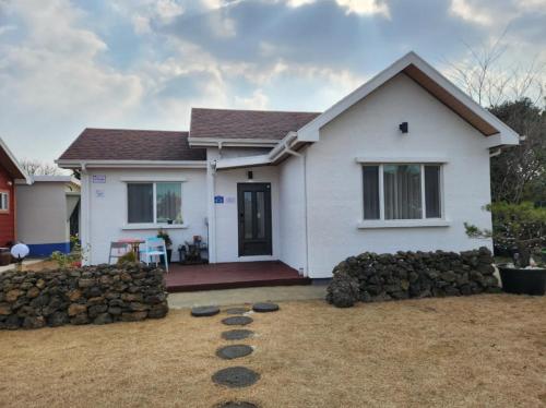 uma casa branca com uma parede de pedra em frente em Sehwa Stay em Jeju