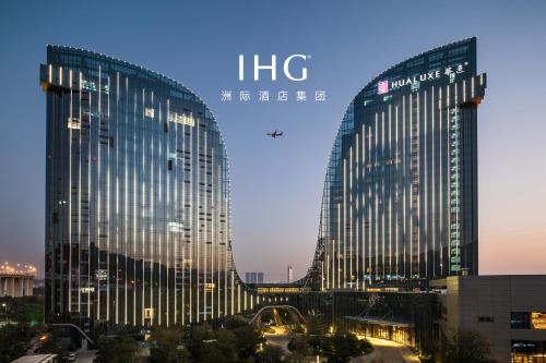 廈門市にあるHUALUXE Xiamen Haicang Habour View - An IHG Hotelの夜の街中の高いガラス張りの建物2棟