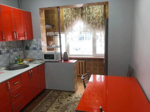uma cozinha com armários vermelhos, um lavatório e uma janela em Айбек 20 em Yakkasaray