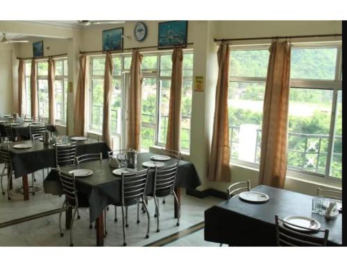 uma sala de jantar com mesas, cadeiras e janelas em Hotel Tulsi, Rudraprayag em Rudraprayāg