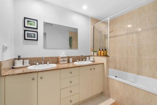 ein Badezimmer mit zwei Waschbecken, einem Spiegel und einer Badewanne in der Unterkunft The Nest Cairns - 4 pools BBQ & Resort in Cairns North