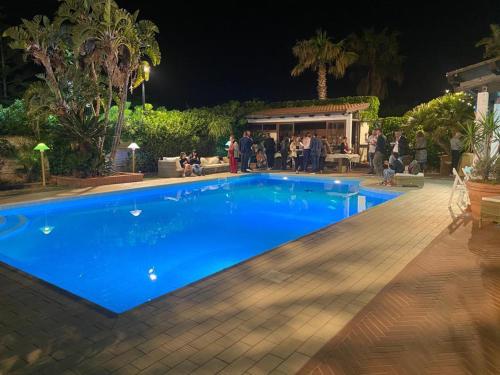 ein blauer Pool in der Nacht mit herumstehenden Leuten in der Unterkunft Villa Seven Palms in Isola delle Femmine