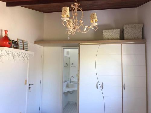 uma casa de banho com um lustre e armários brancos em Casa em Arraial d’Ajuda em Porto Seguro