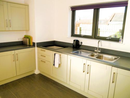 uma cozinha com armários brancos, um lavatório e uma janela em The Longhouse em Castle Douglas