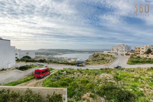 Un camion rosso che guida lungo una strada vicino al fiume di Top of the world 2BR home with spectacular views by 360 Estates a Mellieħa