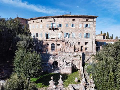 un grand bâtiment en briques sur une colline arborée dans l'établissement Castello di Sovicille - Residenza d'Epoca, à Sovicille