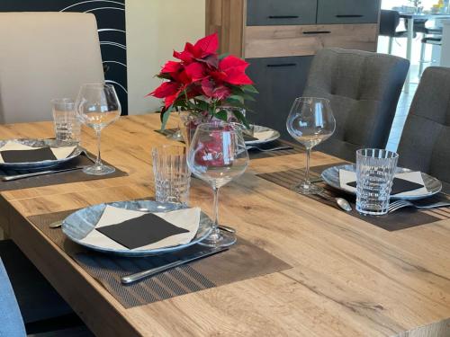 a wooden table with glasses and a vase with red flowers at Le Petit Bonheur in Sergeac
