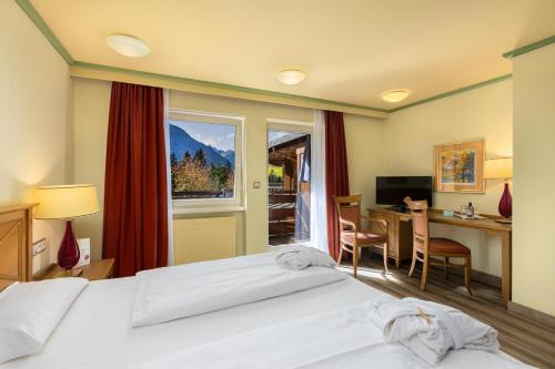 ミッテルベルクにあるIFA Alpenhof Wildental Hotel Kleinwalsertal Adults onlyのベッド、デスク、窓が備わるホテルルームです。