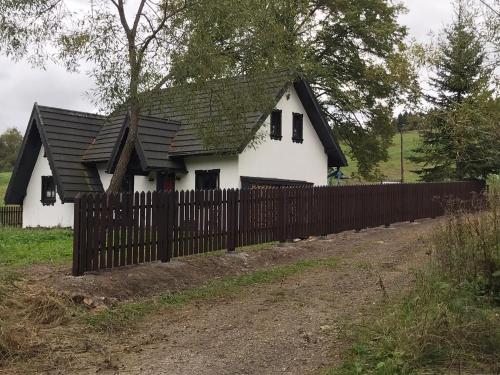 a white house with a black roof behind a fence at Szczęśliwy Domek in Wetlina