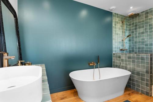 La salle de bains est pourvue d'une baignoire blanche et d'un mur bleu. dans l'établissement Maison face à la mer dans un domaine écologique, à Villerville