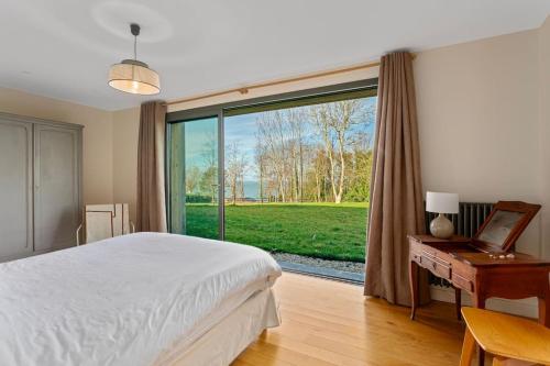 een slaapkamer met een bed, een bureau en een groot raam bij Maison face à la mer dans un domaine écologique in Villerville